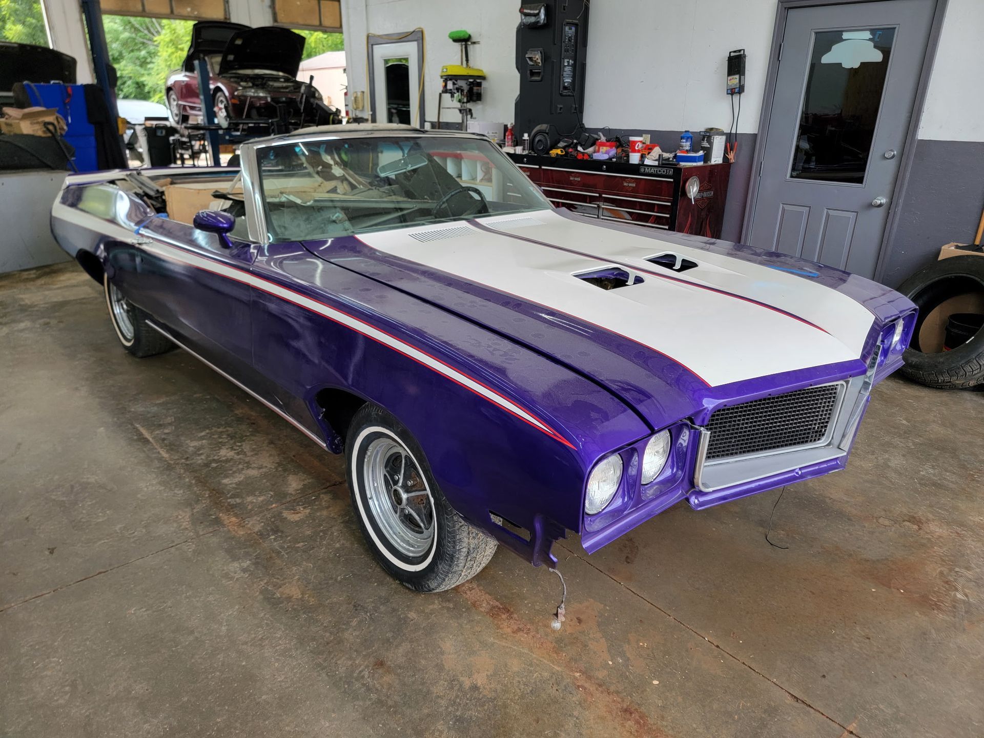 Purple and white convertible car in a garage, hood open, front end stripped, undergoing restoration.