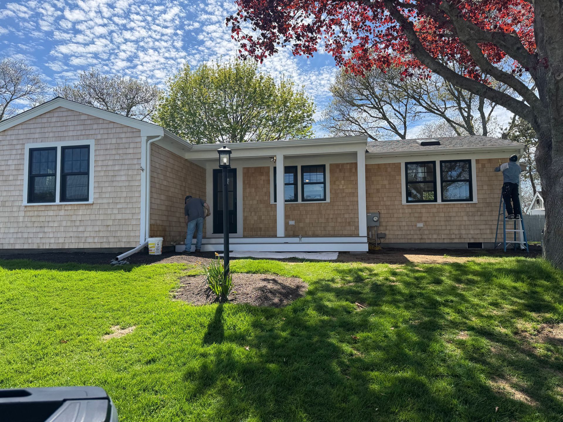 A man is standing on a ladder in front of a house that is being painted.