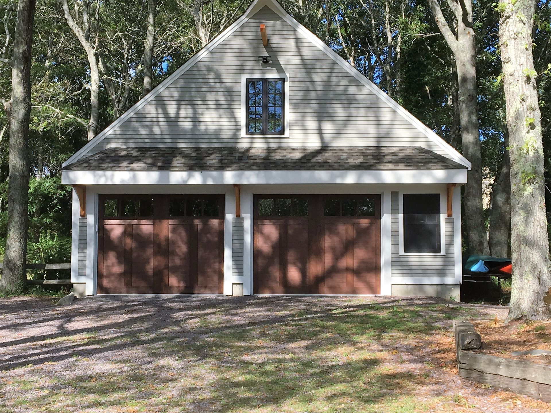 A white garage with brown doors is surrounded by trees.