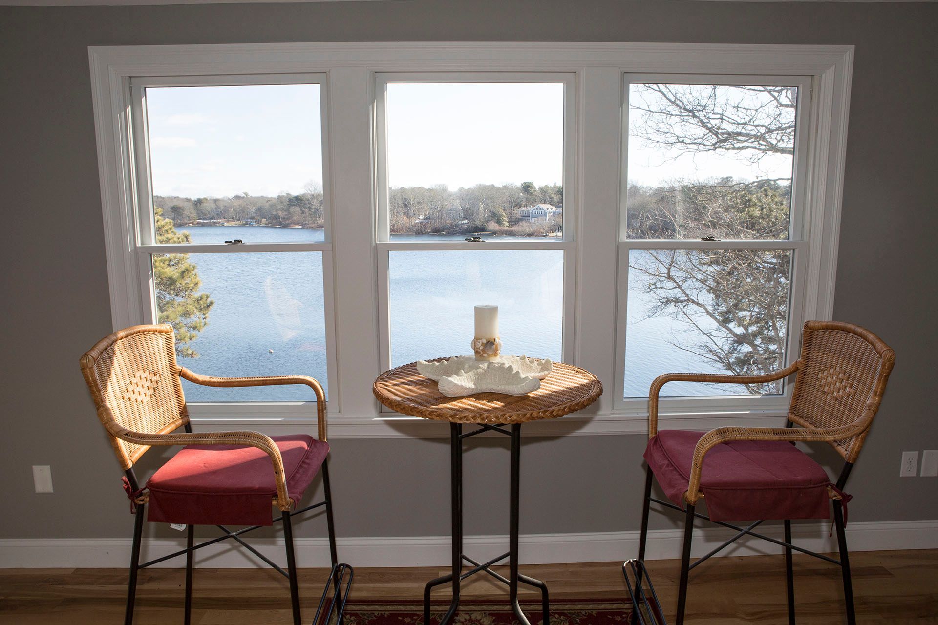 Two chairs and a table in front of a window overlooking a lake.
