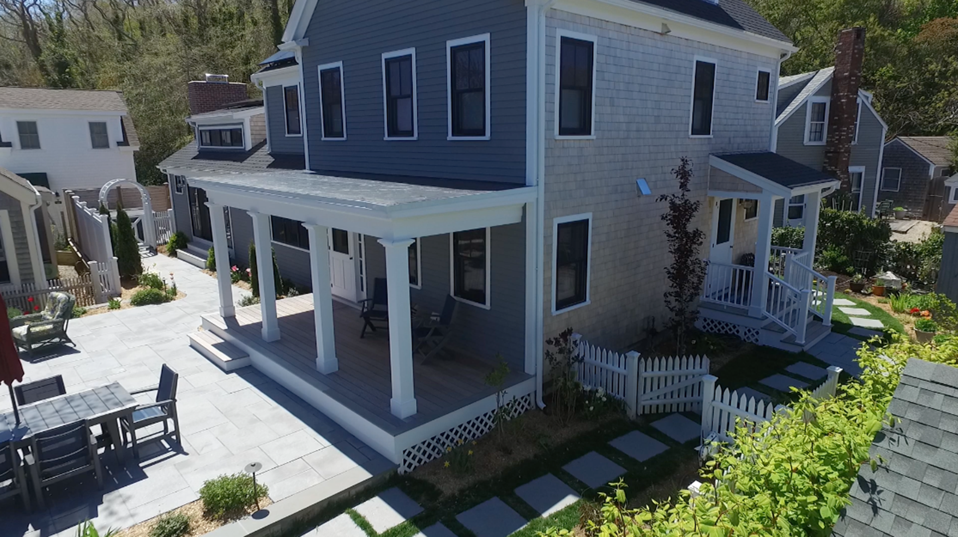 Gray and blue house with white porch and picket fence; outdoor seating area and walkway.