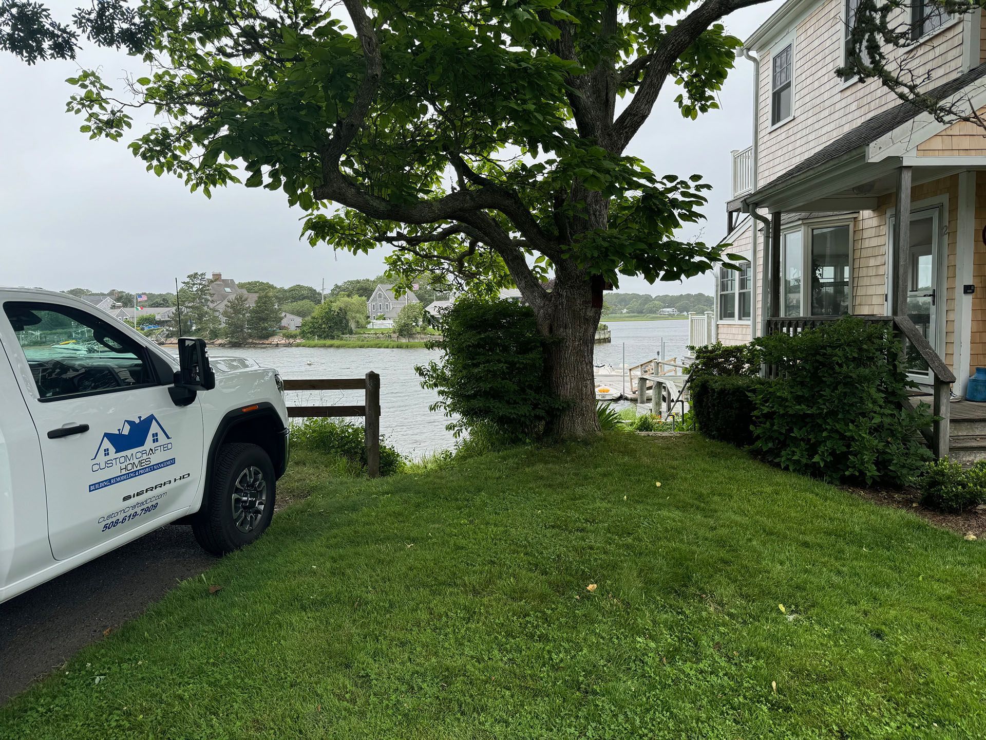 A white truck is parked in front of a house next to a body of water.