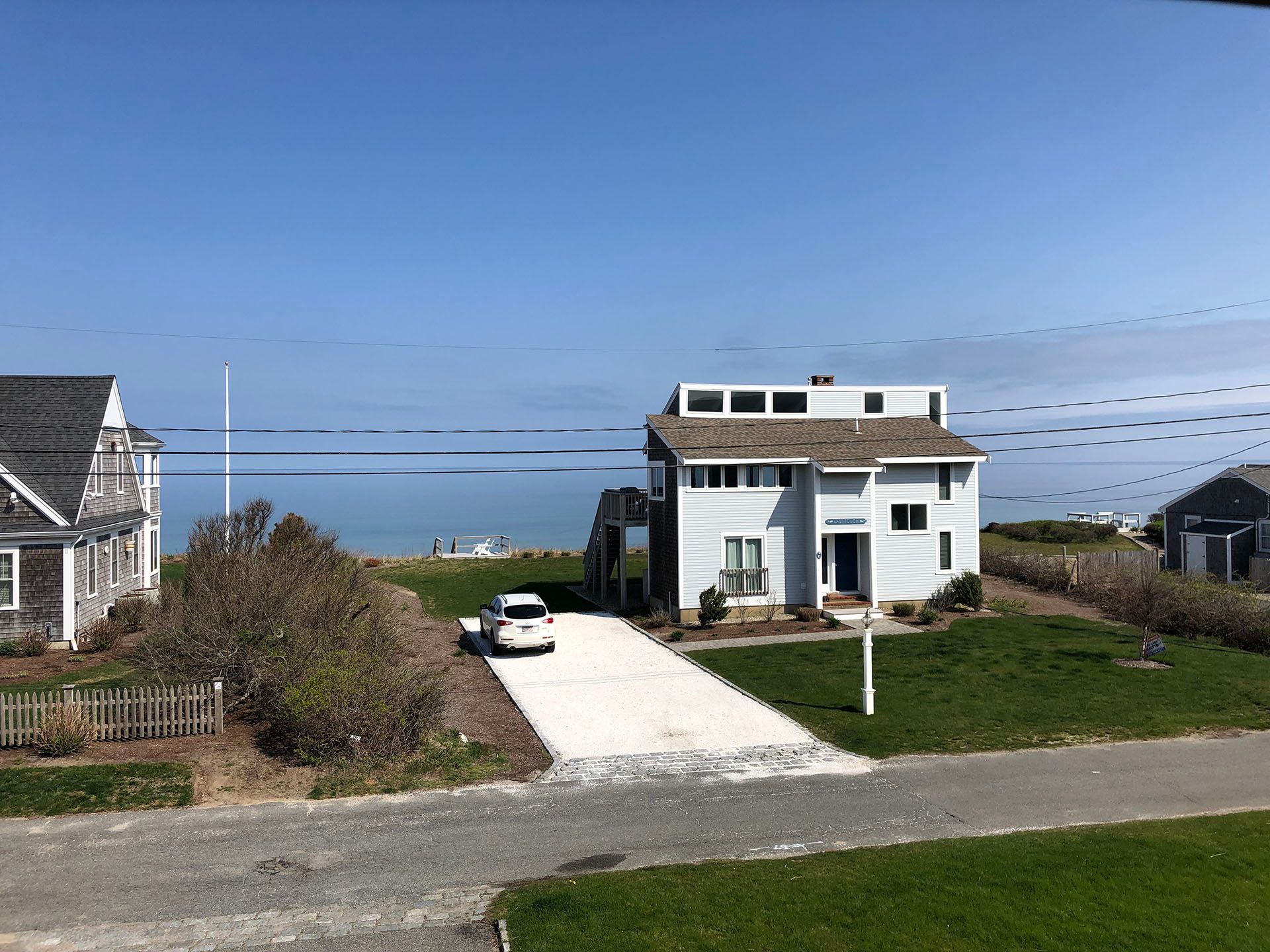 A white house with a car parked in front of it and a view of the ocean.