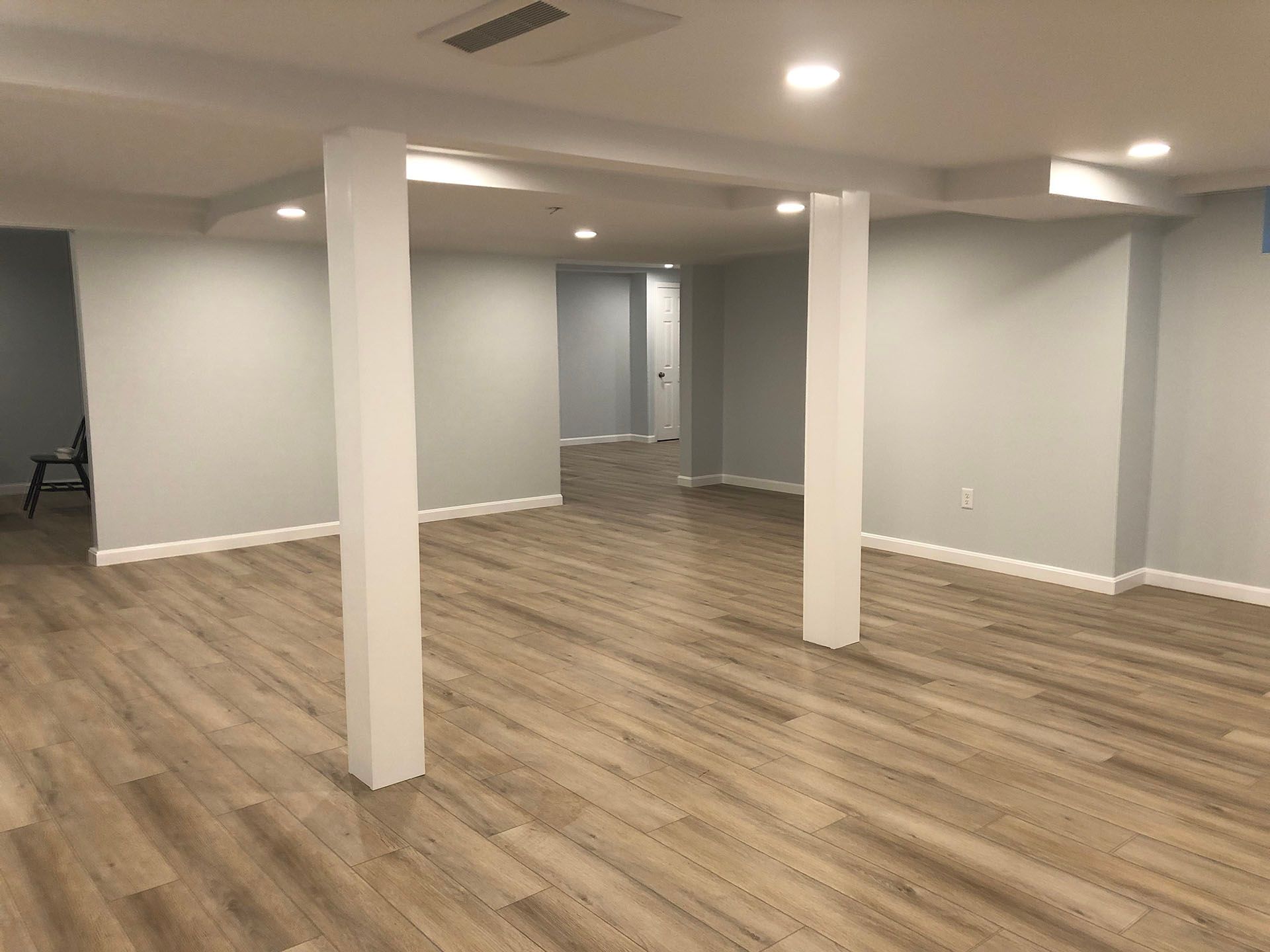 An empty basement with hardwood floors and white pillars.