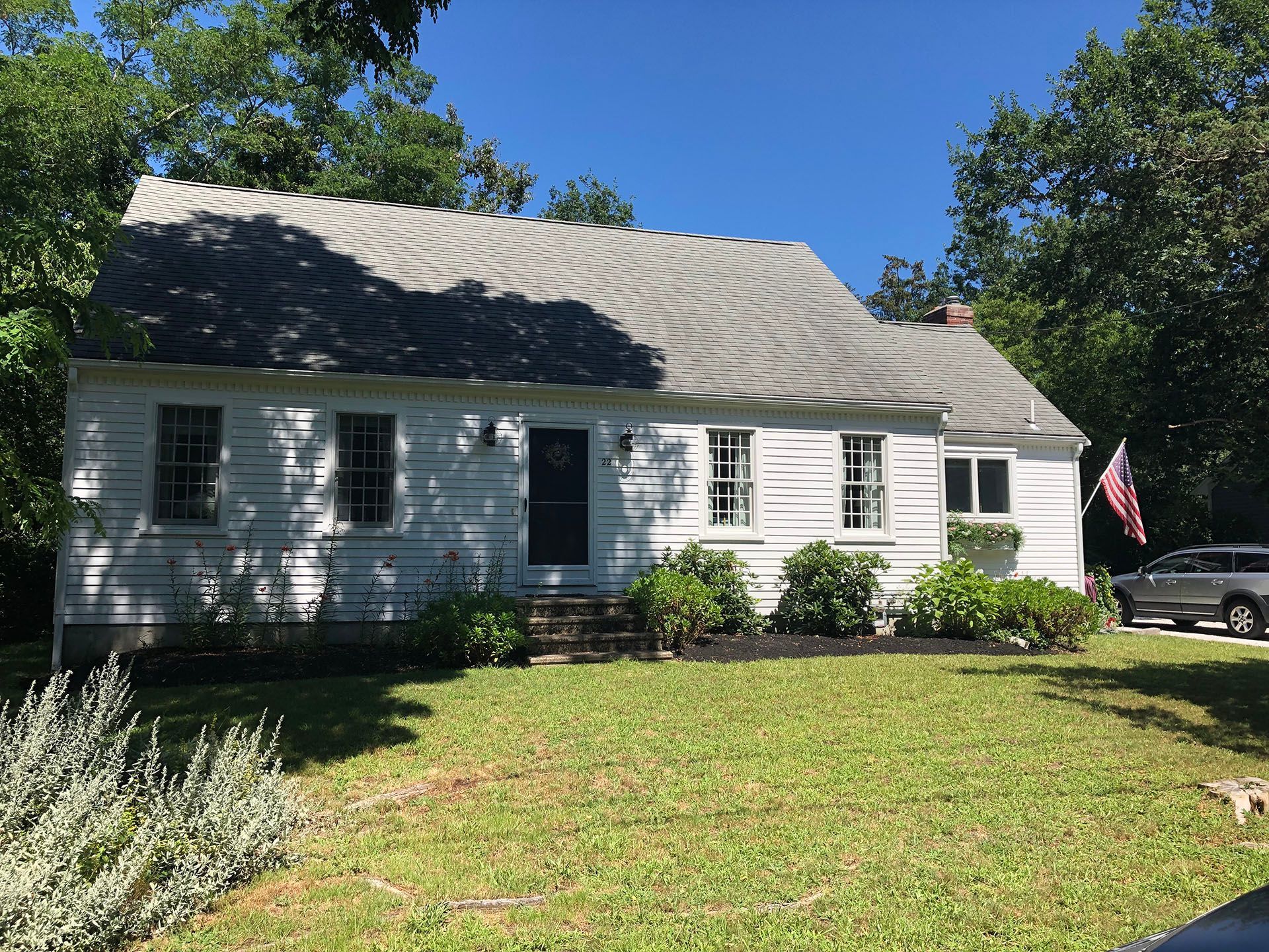 A white house with a gray roof is sitting on top of a lush green lawn.