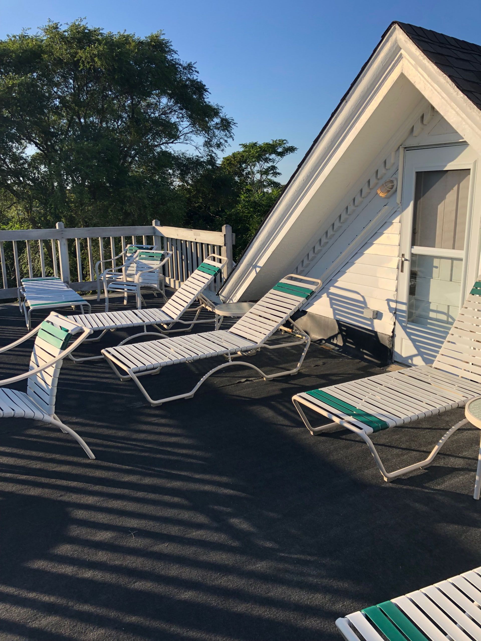 White and green lounge chairs on a rooftop deck with a white building in the background under a clear, blue sky.