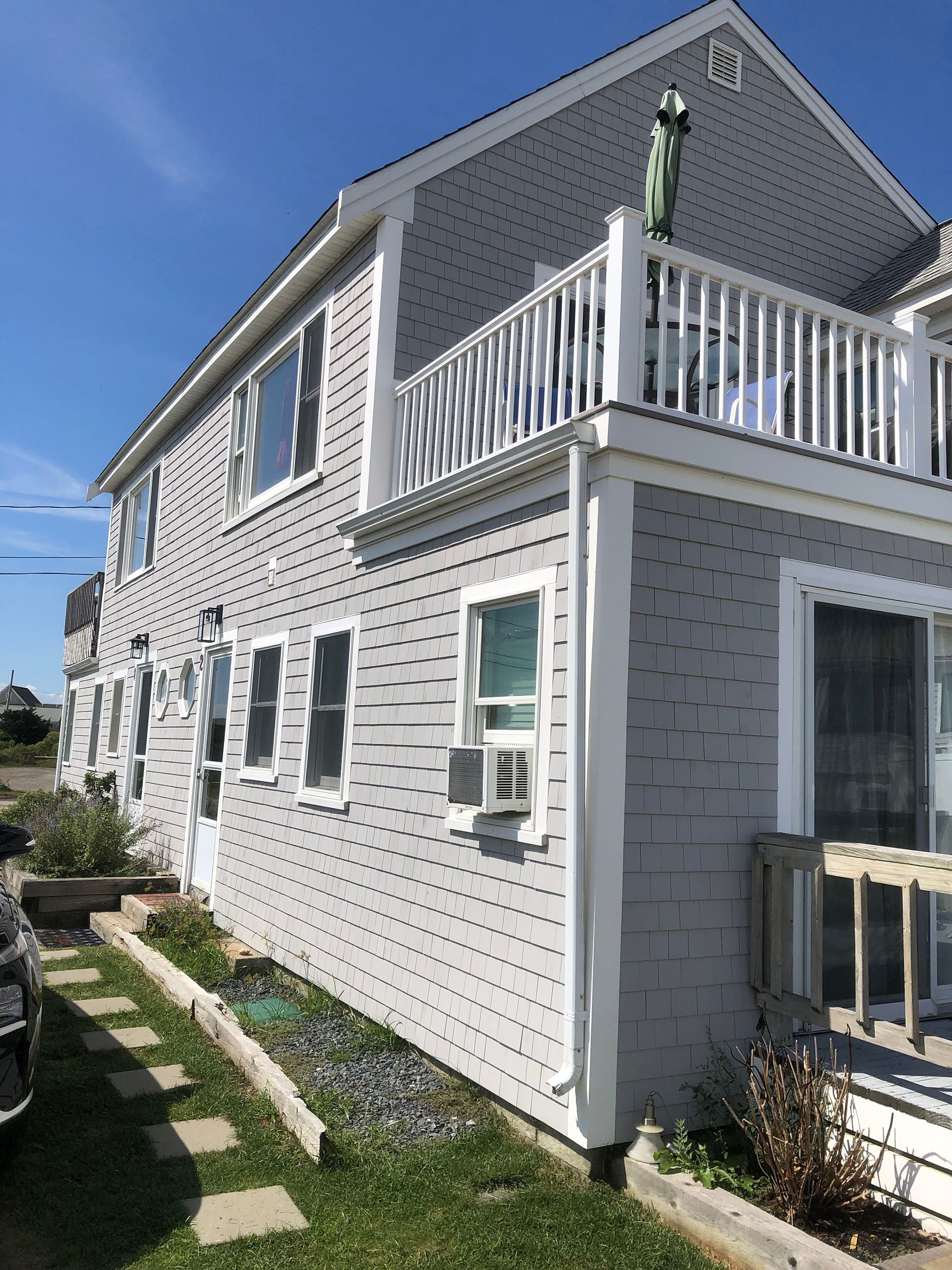 A large gray house with a balcony and a car parked in front of it.