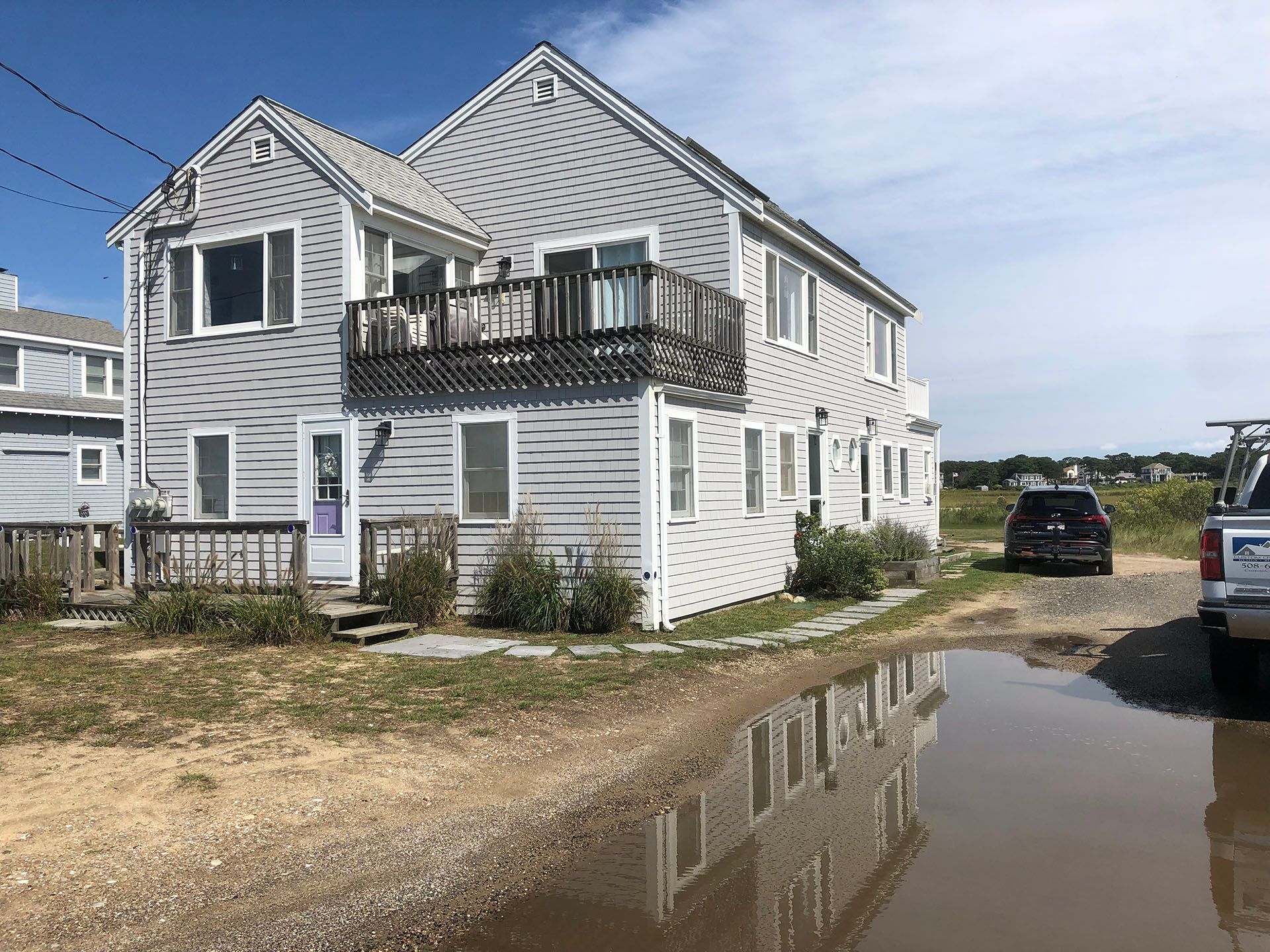 A house with a car parked in front of it and a puddle of water in front of it.