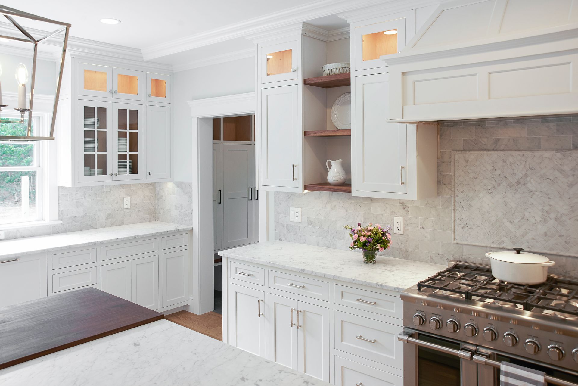 White kitchen with marble countertops, stainless steel stove, and open shelves.