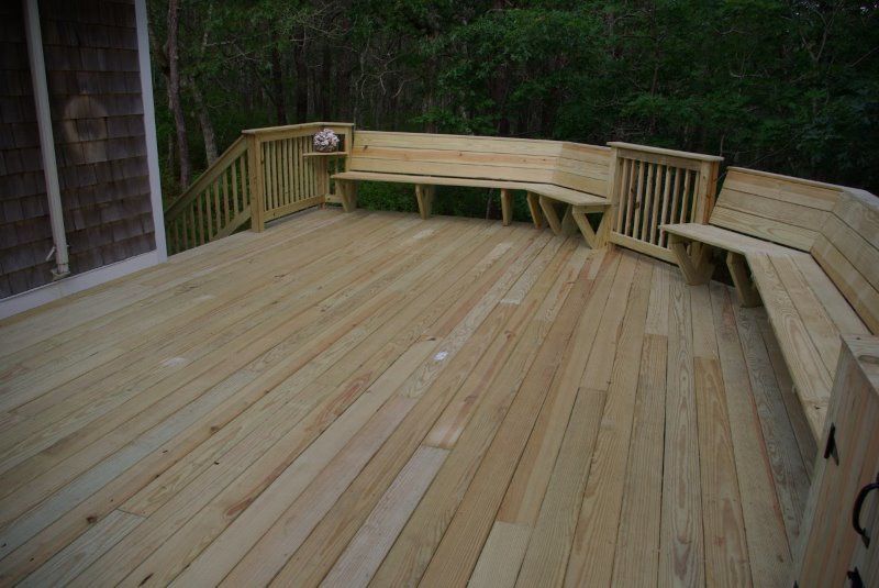Wooden deck with built-in benches, near a house and trees.