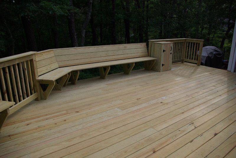 Wooden deck with built-in bench and railing, set in a wooded area.