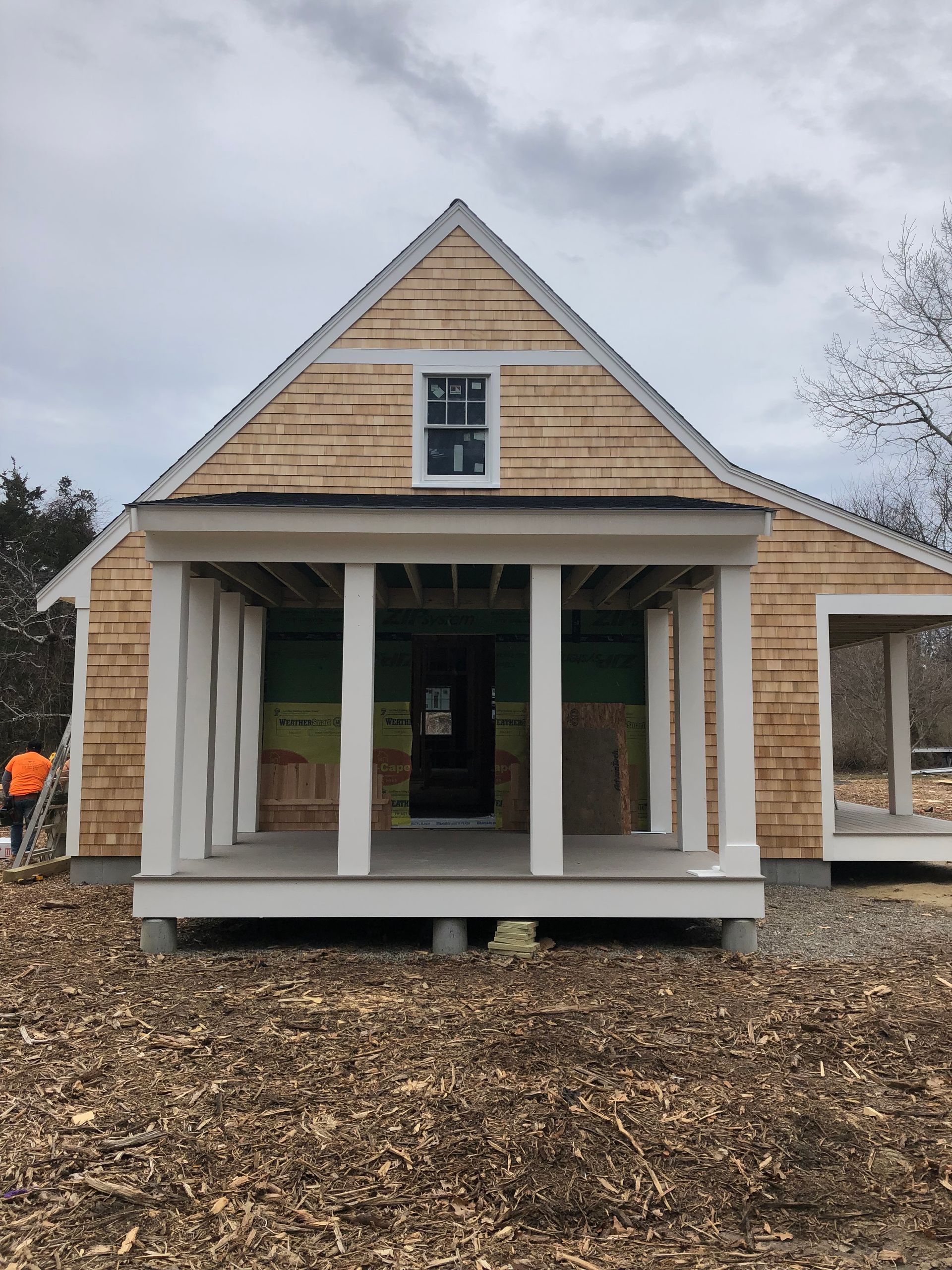 A small, unfinished house with a porch and light-colored wood siding against a cloudy sky.