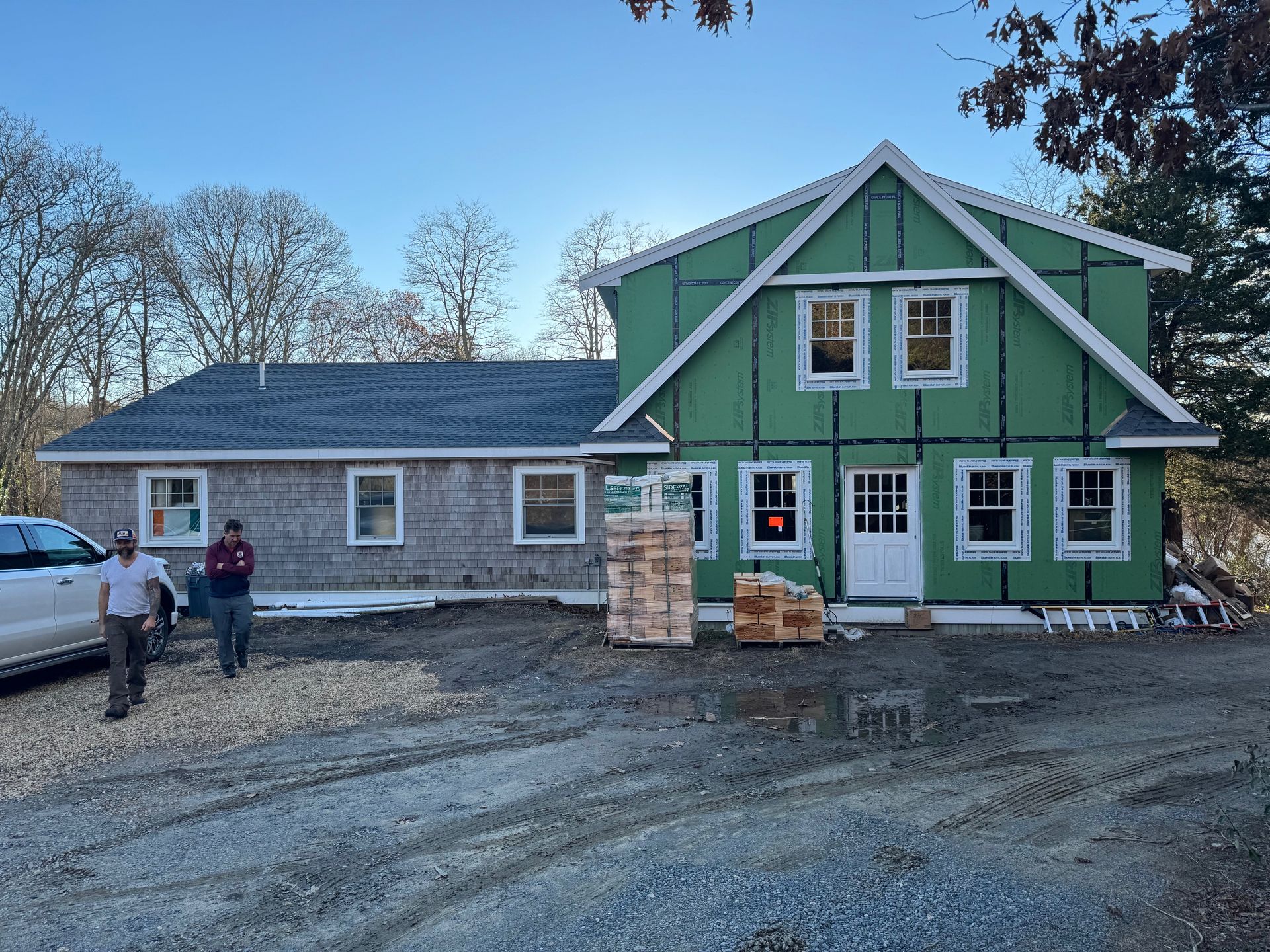 Two men are standing in front of a green house under construction.