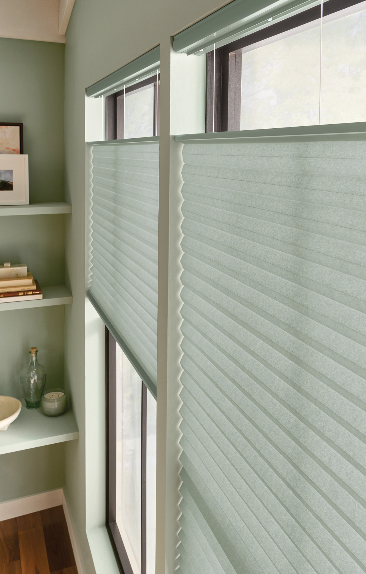Light green cellular shades covering tall windows in a soft green room