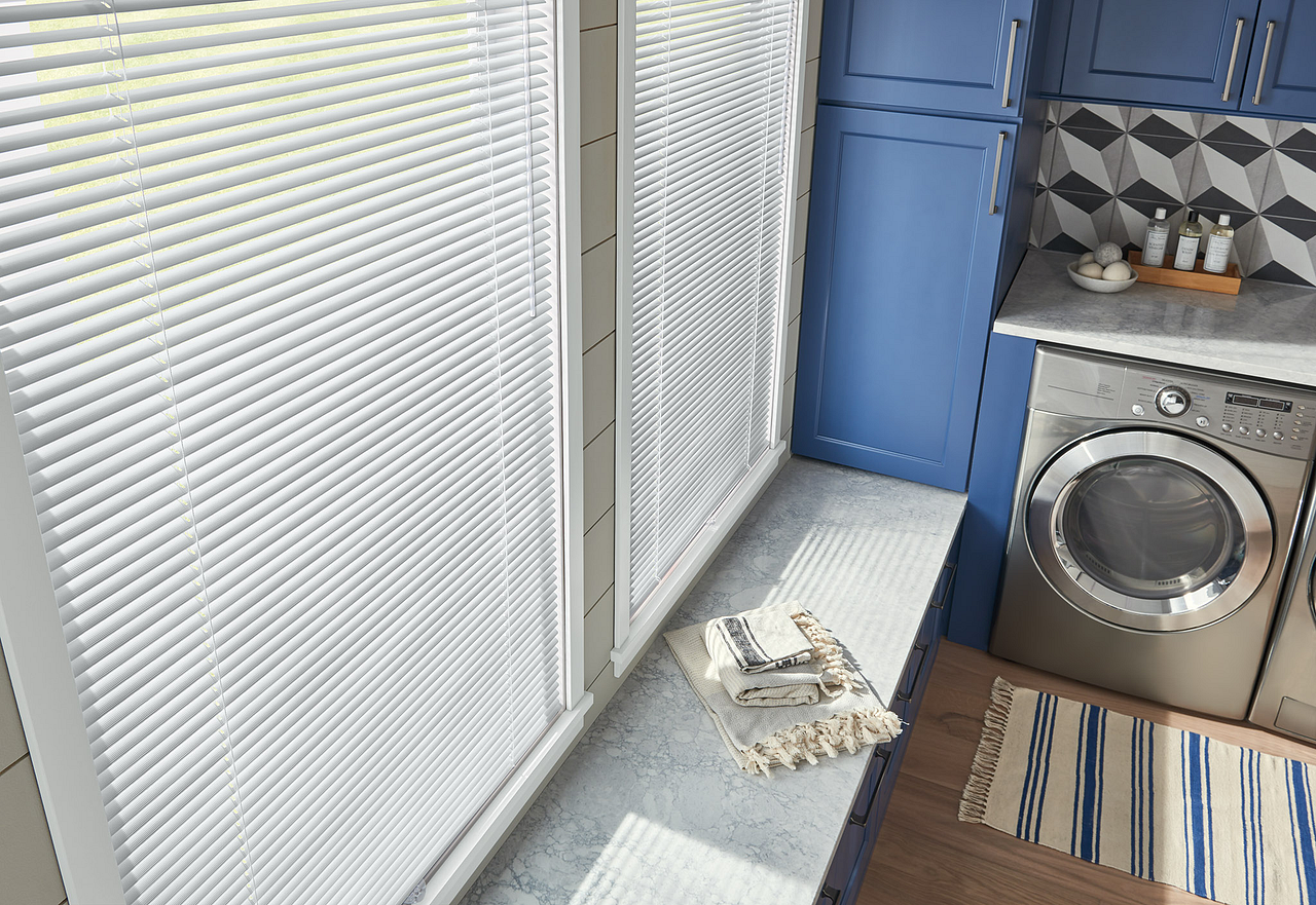Bright kitchen with window blinds, blue cabinets, washing machine, and a tray on the sill.