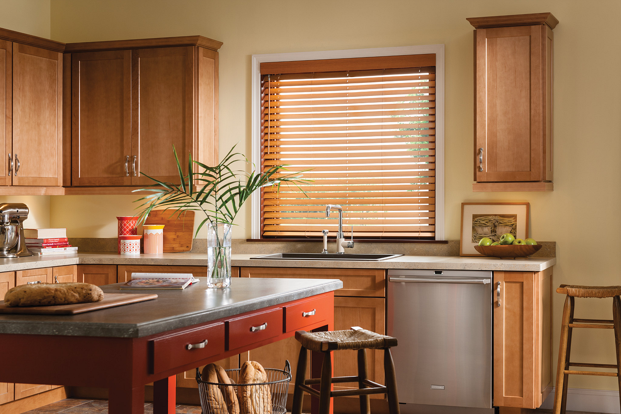 Bright kitchen with wooden cabinets, island, sink under window blinds, and dishwasher.