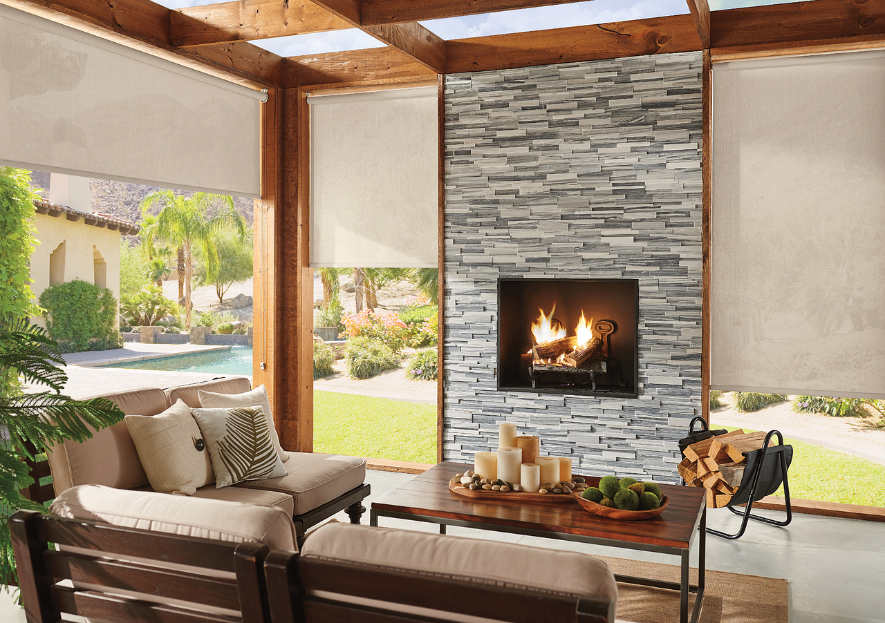 Cozy patio living room with stone fireplace, cushioned chairs, and outdoor view through open walls