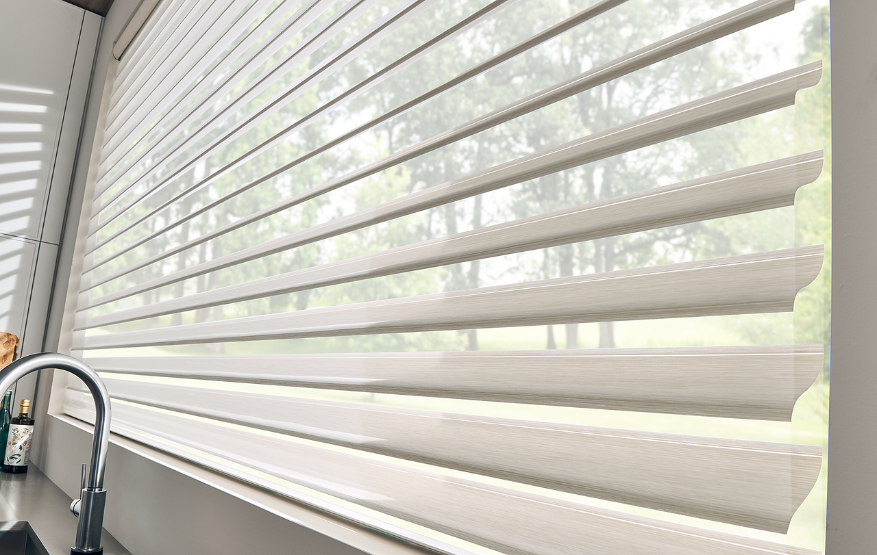 White horizontal window blinds lit by sunlight beside a kitchen faucet