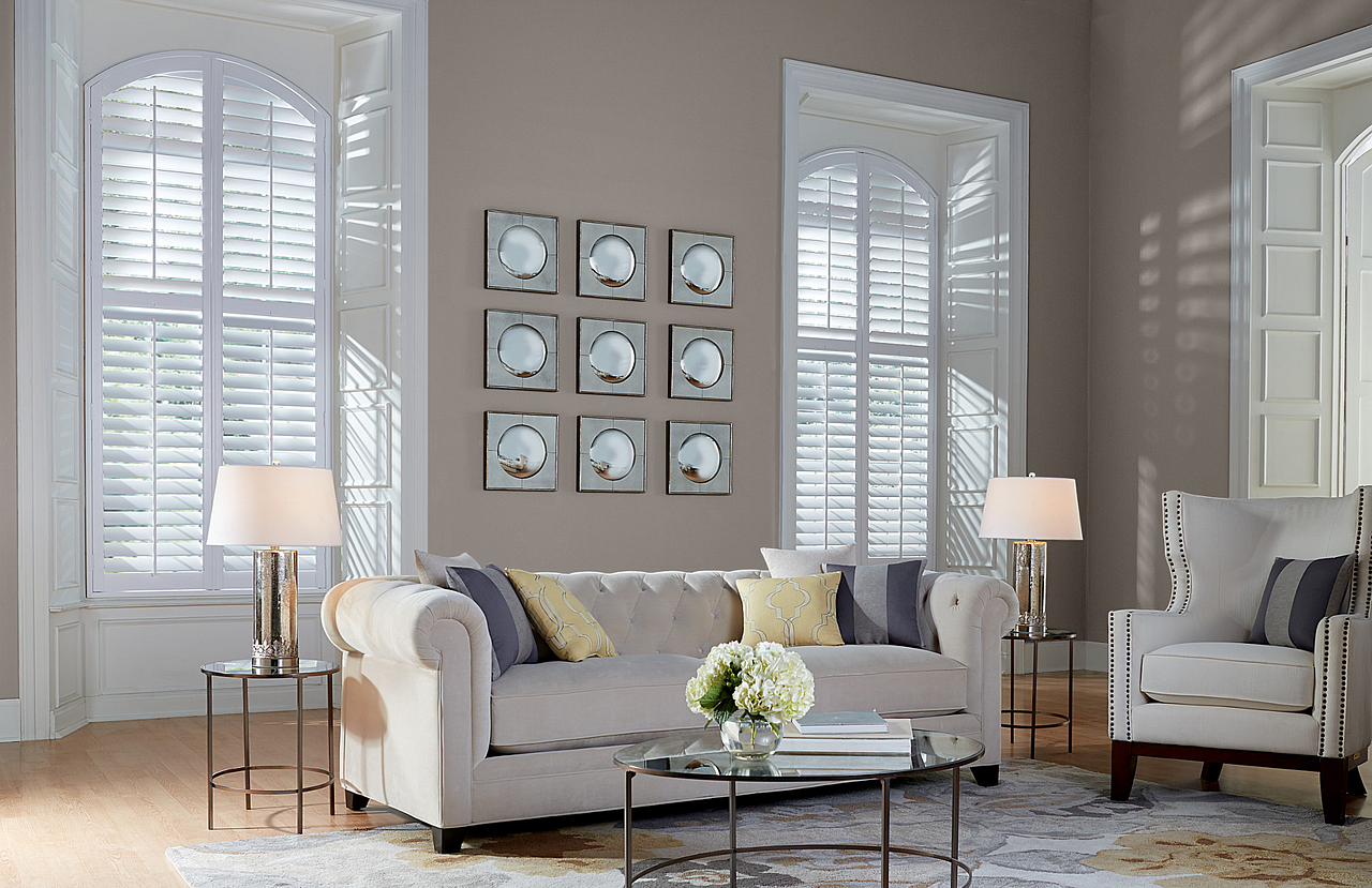 Bright living room with white sofas, floor lamps, large windows, and framed wall art