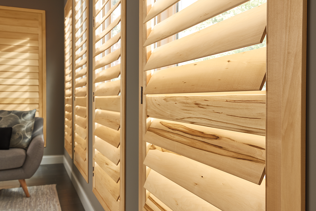 Wooden window shutters lit by warm sunlight beside a gray armchair in a modern room