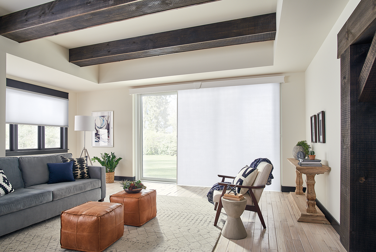 Bright living room with gray sofa, wooden chairs, and large sliding glass doors letting in daylight