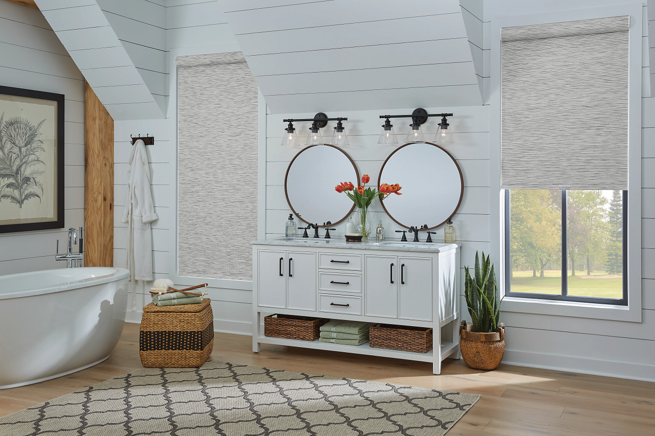 Bright bathroom with freestanding tub, white vanity with round mirrors, woven baskets, and large windows