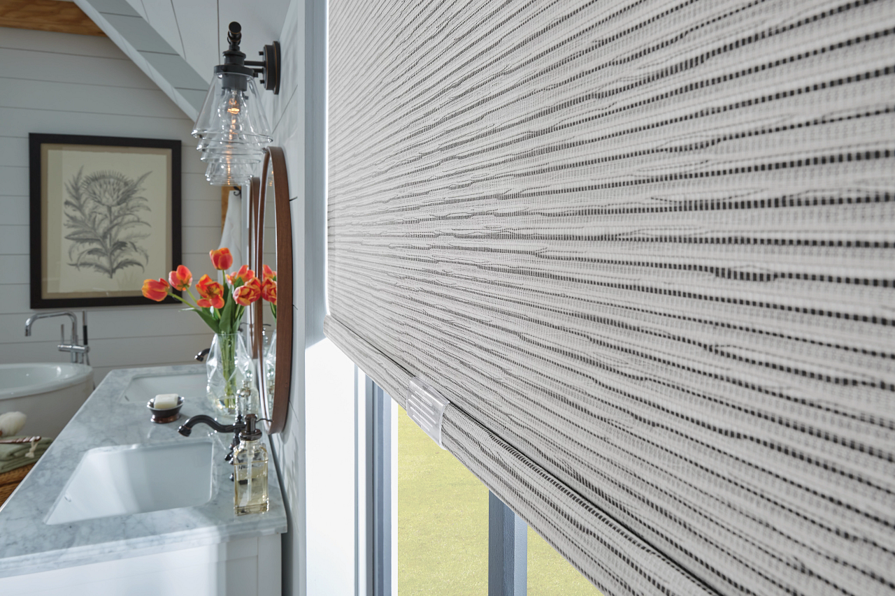 Modern bathroom with a large textured window shade, white vanity, and orange flowers in a vase