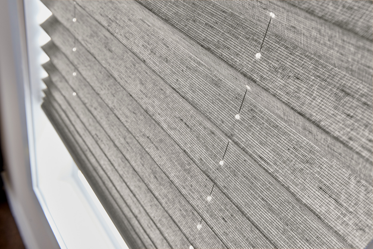 Close-up of gray pleated window blinds with small white specks near a window frame