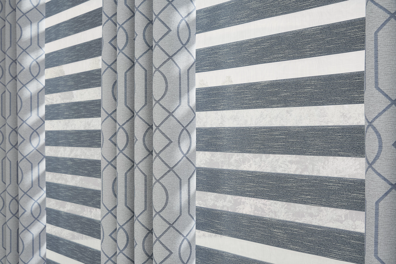Gray striped curtains with a geometric-patterned sheer panel hanging by a window