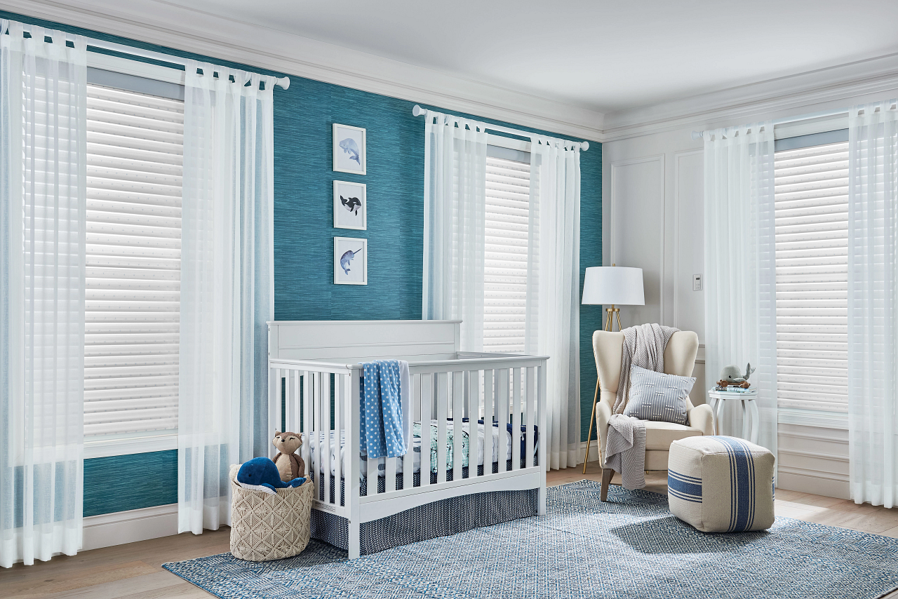 Nursery with white crib, teal accent wall, striped rug, and cozy chair by bright windows