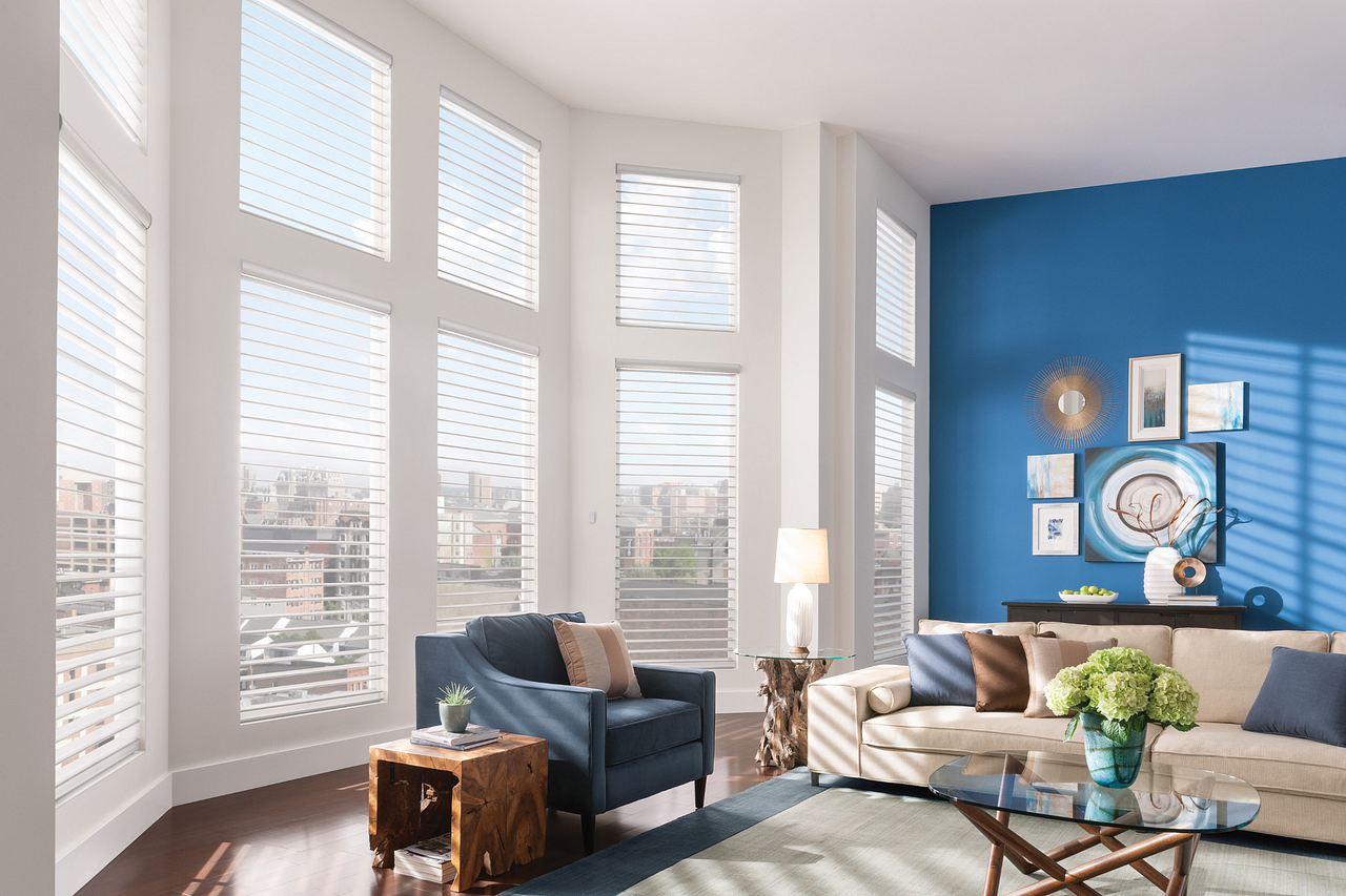 Bright living room with tall windows, blue accent wall, sofa, armchair, and coffee table with flowers