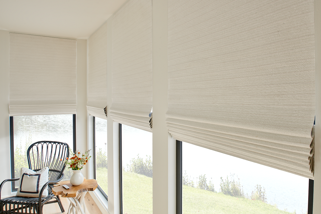 Bright sunroom with woven blinds, wicker chairs, and potted plants by large windows.