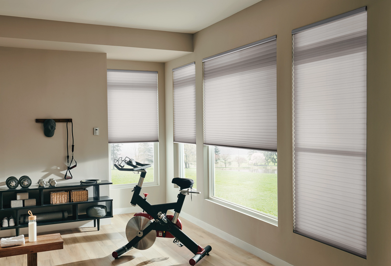 Home gym with a stationary bike by large windows and blinds in a bright room