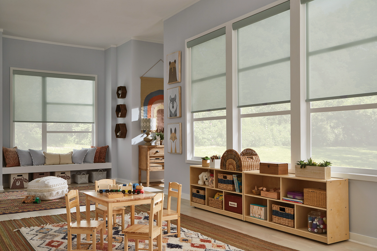 Bright classroom with wooden tables, large windows, and shelves of toys and supplies