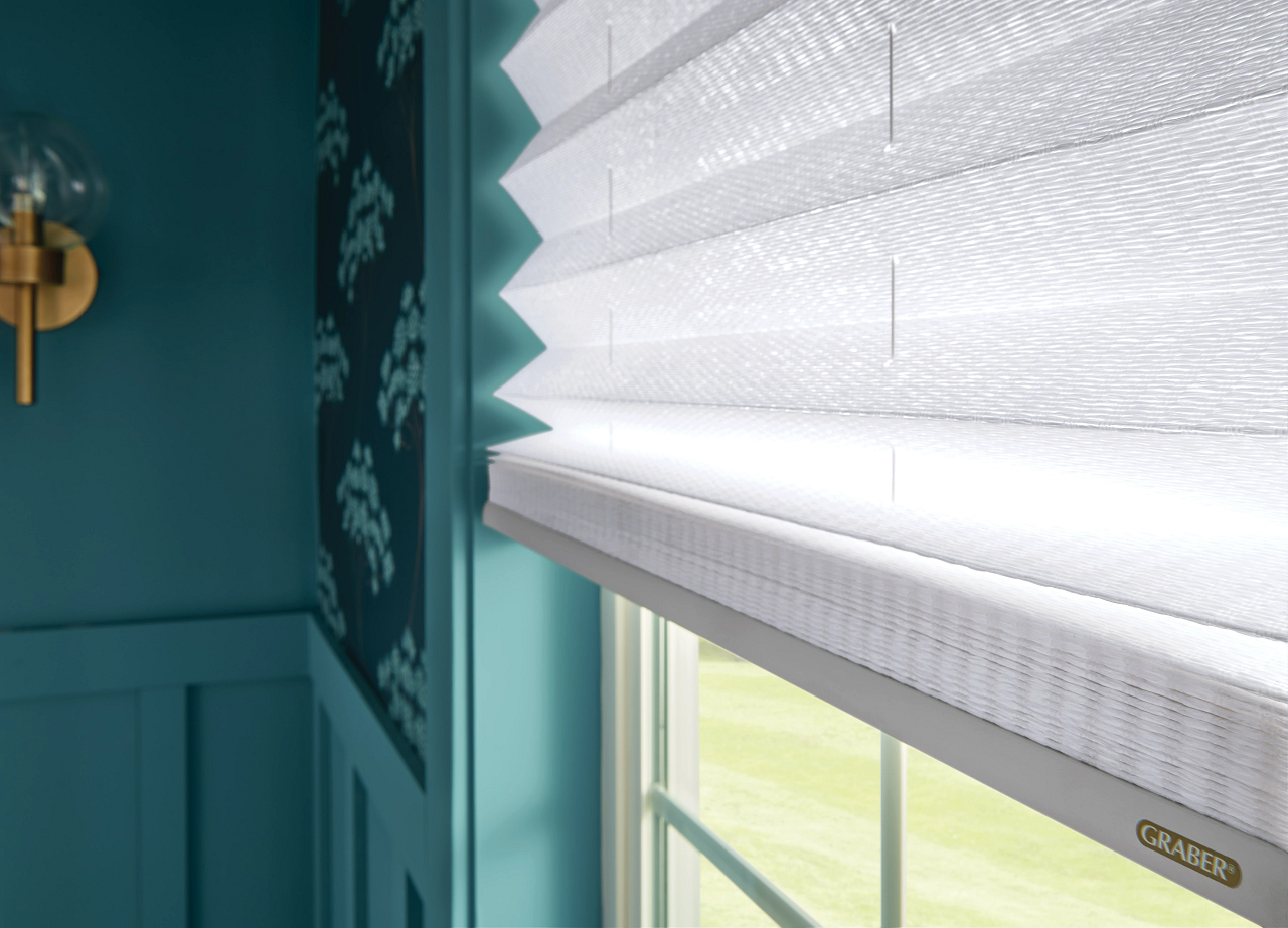 White window blinds in a teal room with sunlight filtering through a window.
