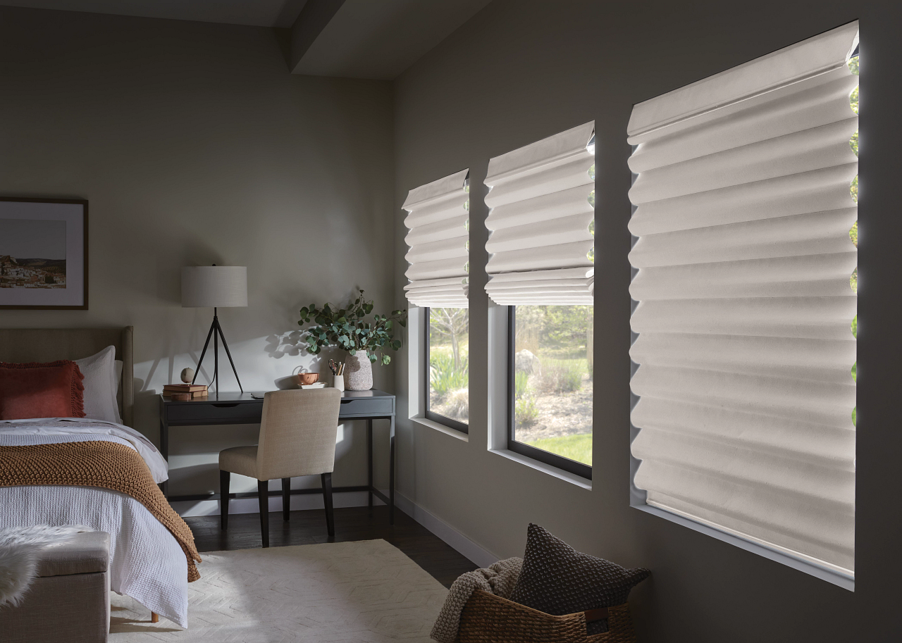 Bright bedroom with a bed, desk, chair, and large windows covered by white blinds.