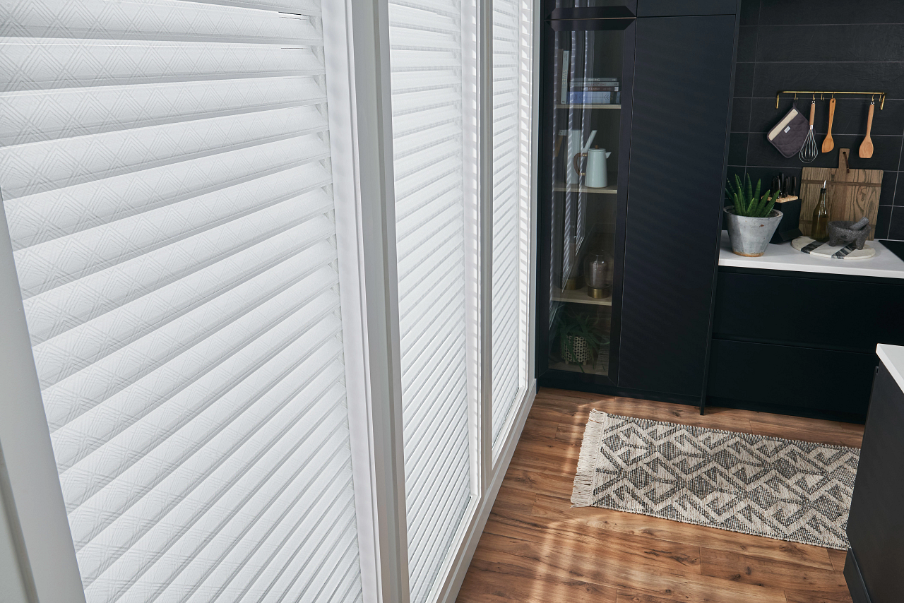 Hallway with white blinds, wood floor, patterned rug, and dark shelving at the end.