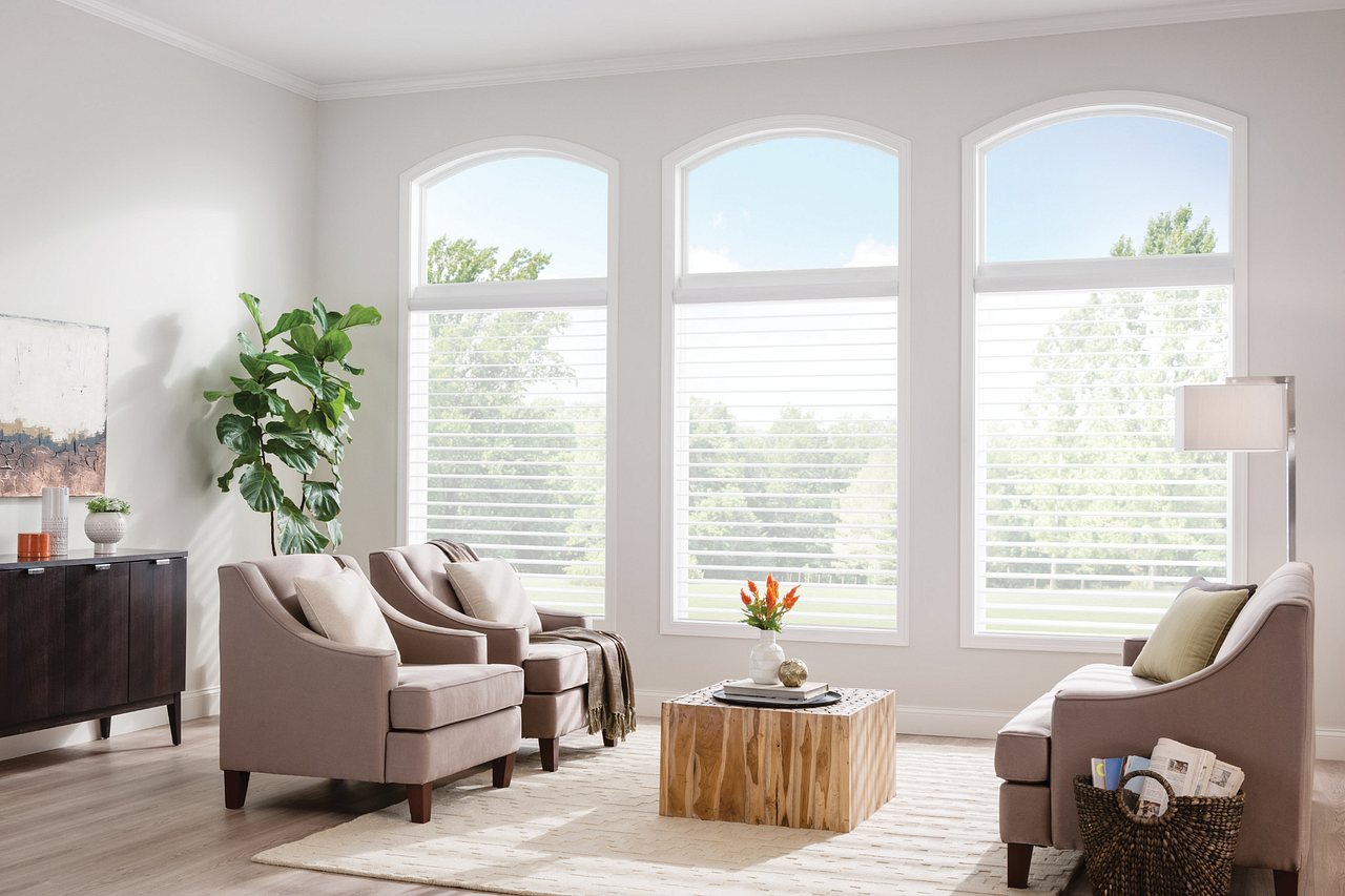 Bright living room with large windows, beige chairs, a wooden coffee table, and a floor lamp.