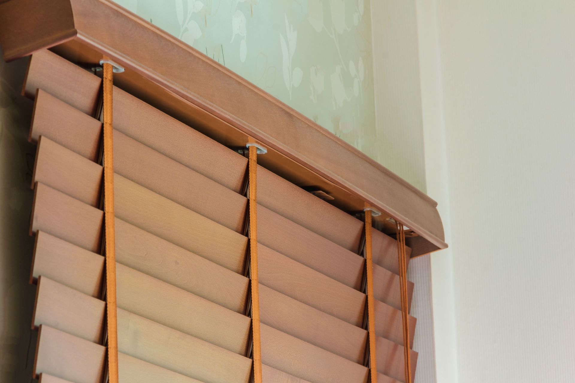 Close-up of brown wooden window blinds with a matching valance against a light wall