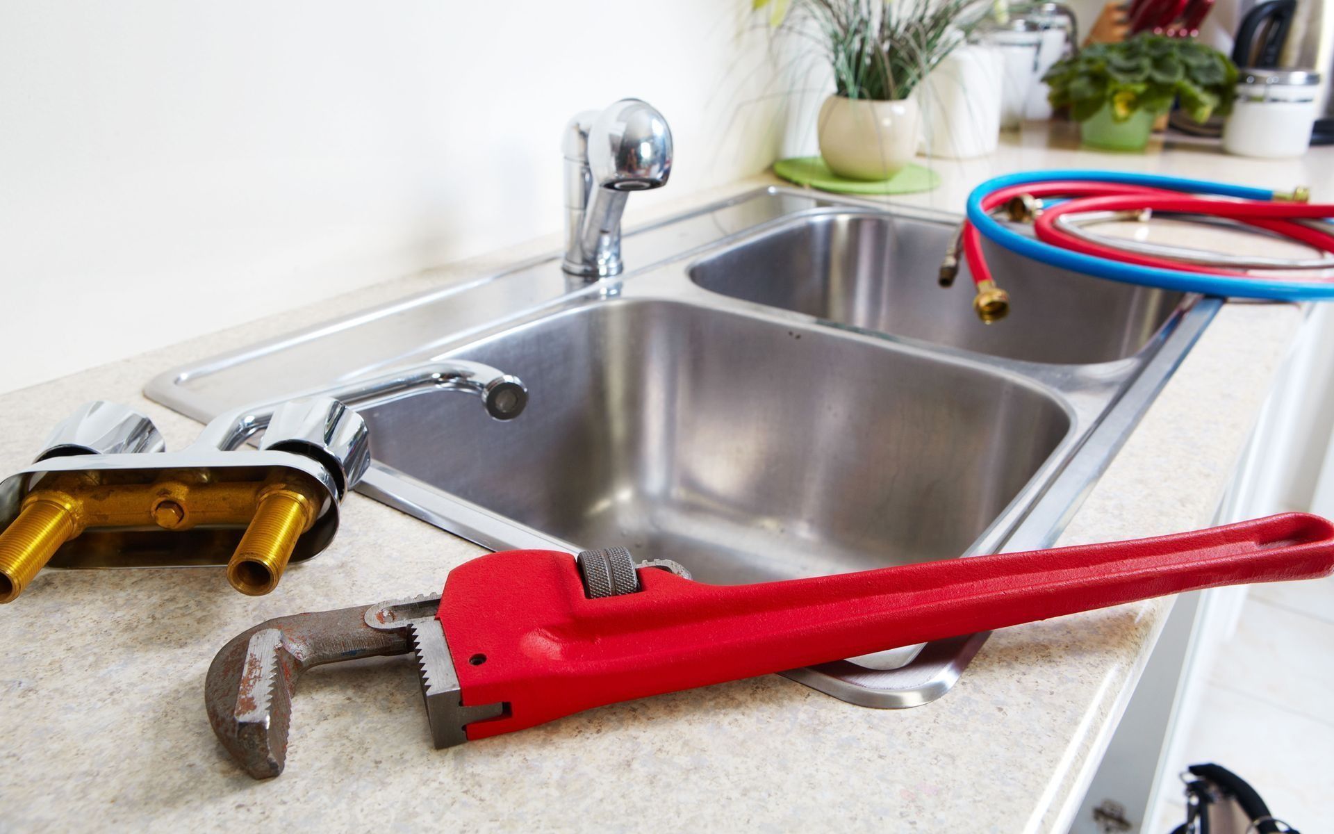 Kitchen sink with plumbing tools; faucet, wrench, and hoses.