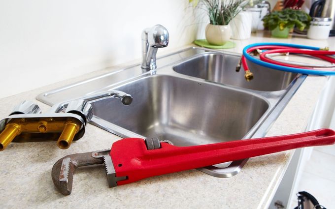 A red pipe wrench and faucet parts next to a double sink; plumbing repair on a countertop.