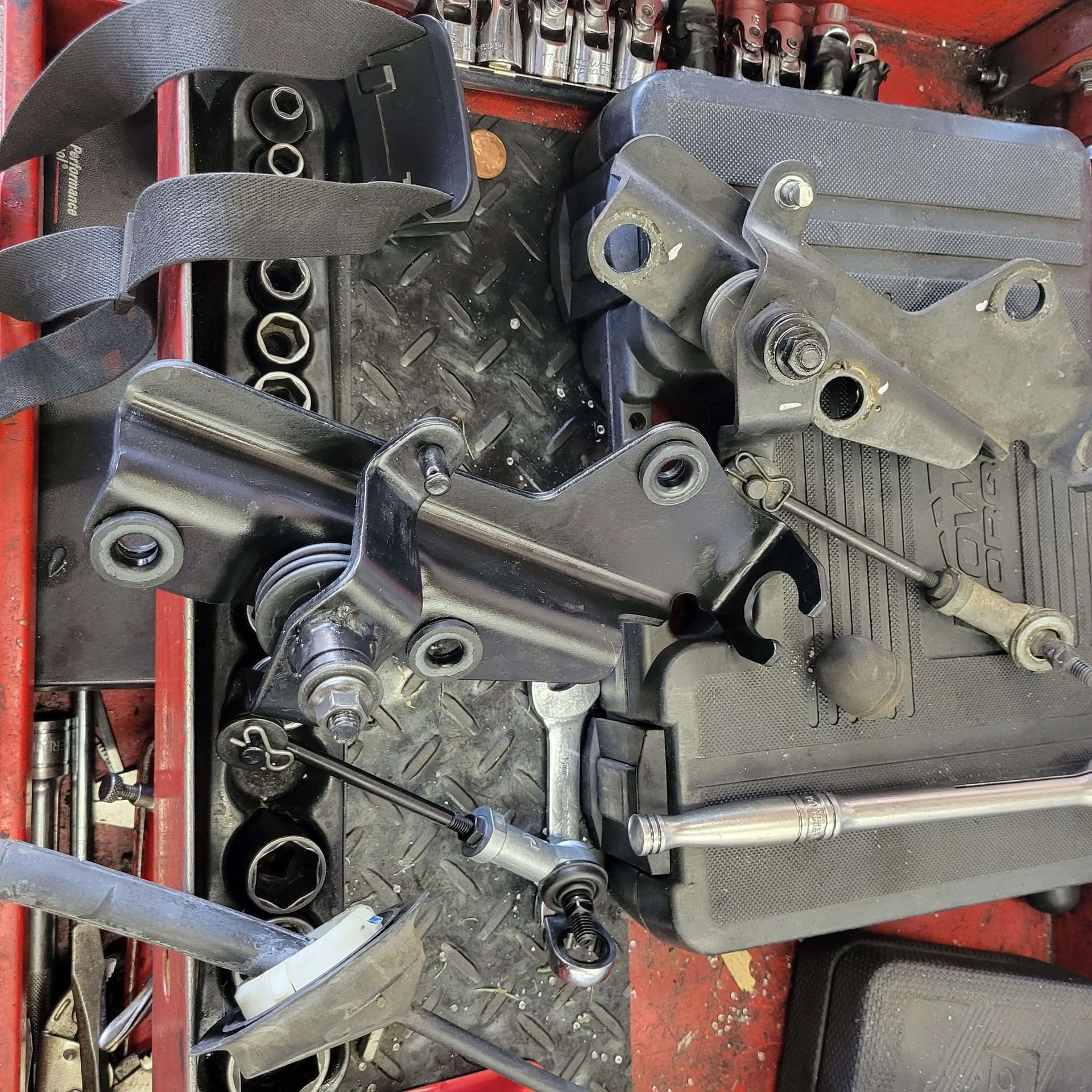Black metal brackets, tools, and hardware arranged on a work surface, possibly a toolbox.