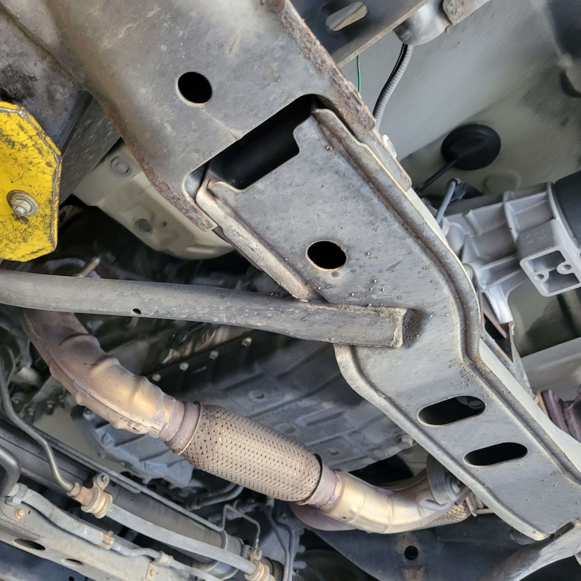 Underside view of a vehicle's frame, exhaust pipe, and transmission, showing metal components and some rust.