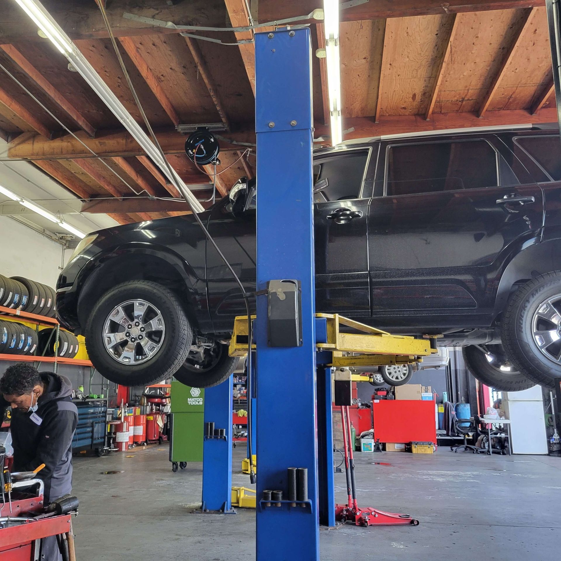 Black SUV raised on a blue car lift inside a garage; a person works underneath.