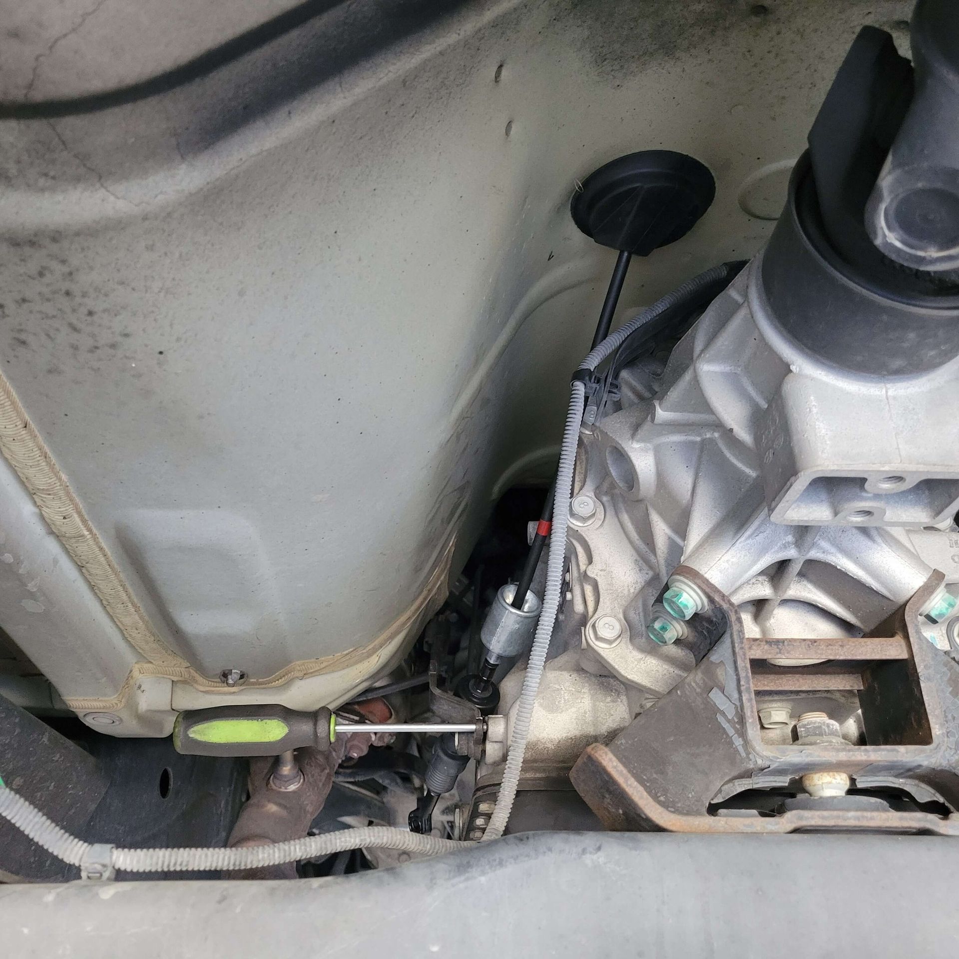 A mechanic's hand using a screwdriver under a vehicle's undercarriage to work on a transmission.