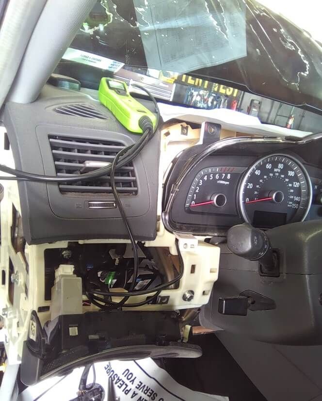 Car dashboard disassembled, electronic tool connected, instrument cluster visible.