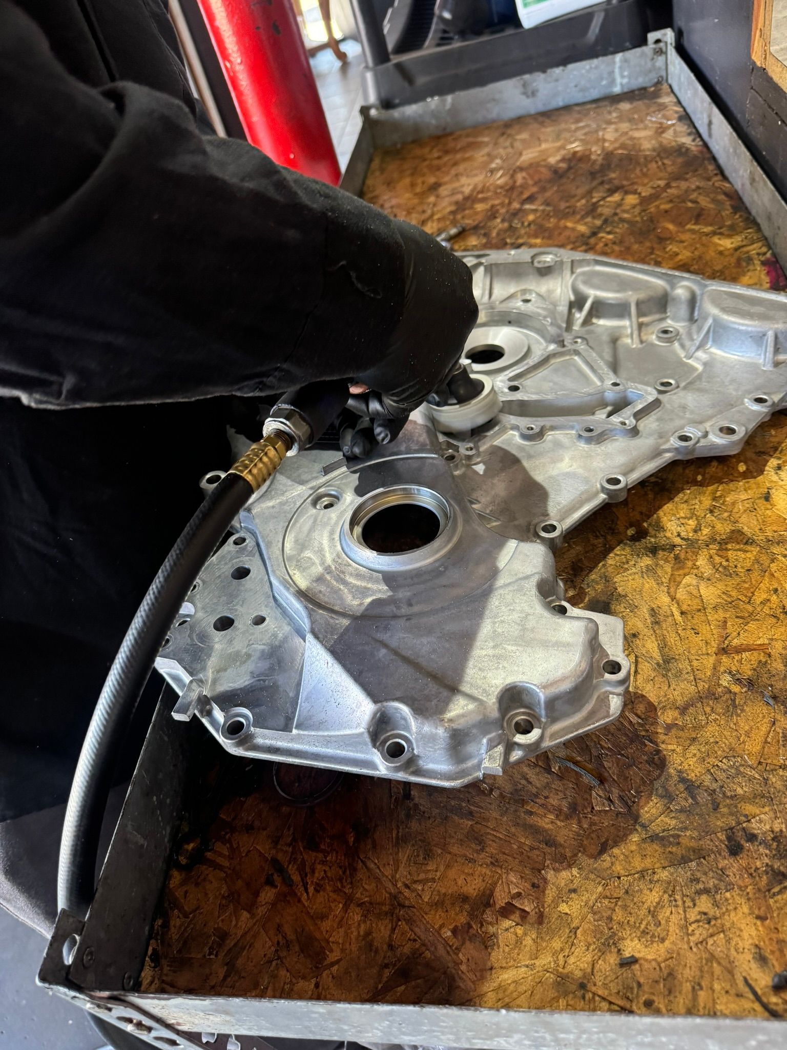 Person using air hose to clean a metal engine part on a workbench.