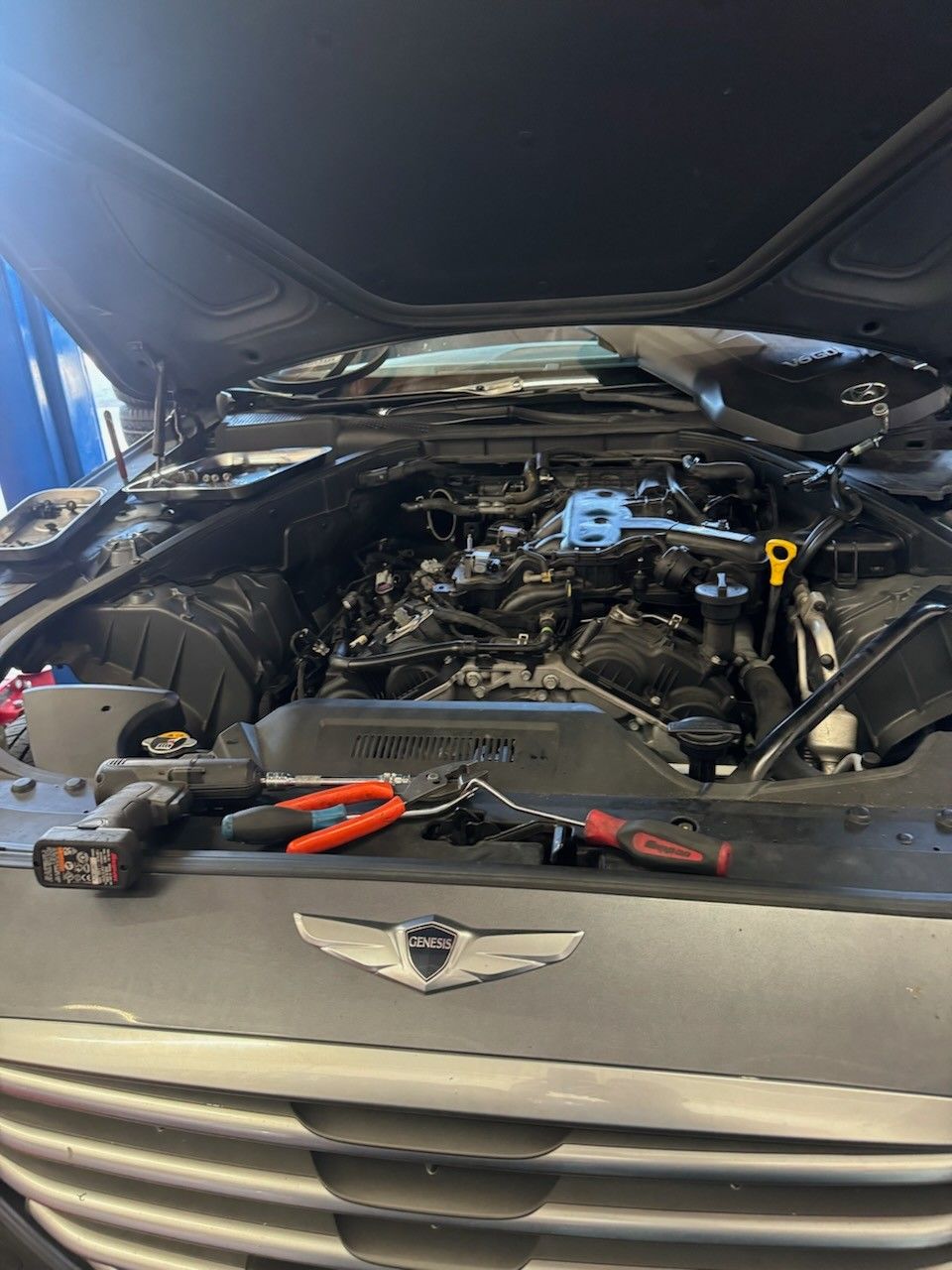 Car engine bay open for service, tools on the bumper.