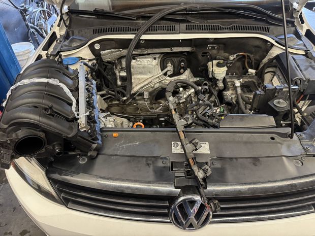 Car engine bay with parts removed, exposed engine components, white car, garage setting.