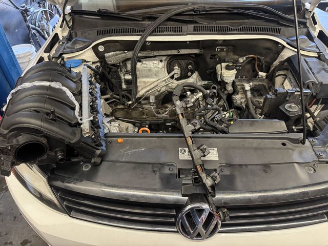 Car engine bay with parts removed, exposed engine components, white car, garage setting.